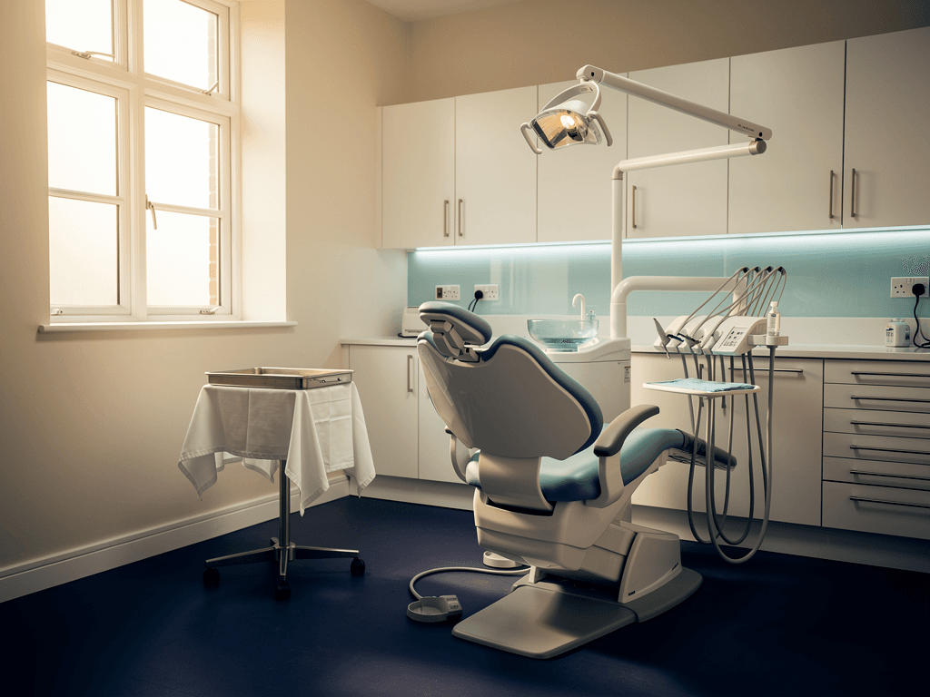 A single empty dental treatment room in a private practice, pale blue chair, late afternoon light